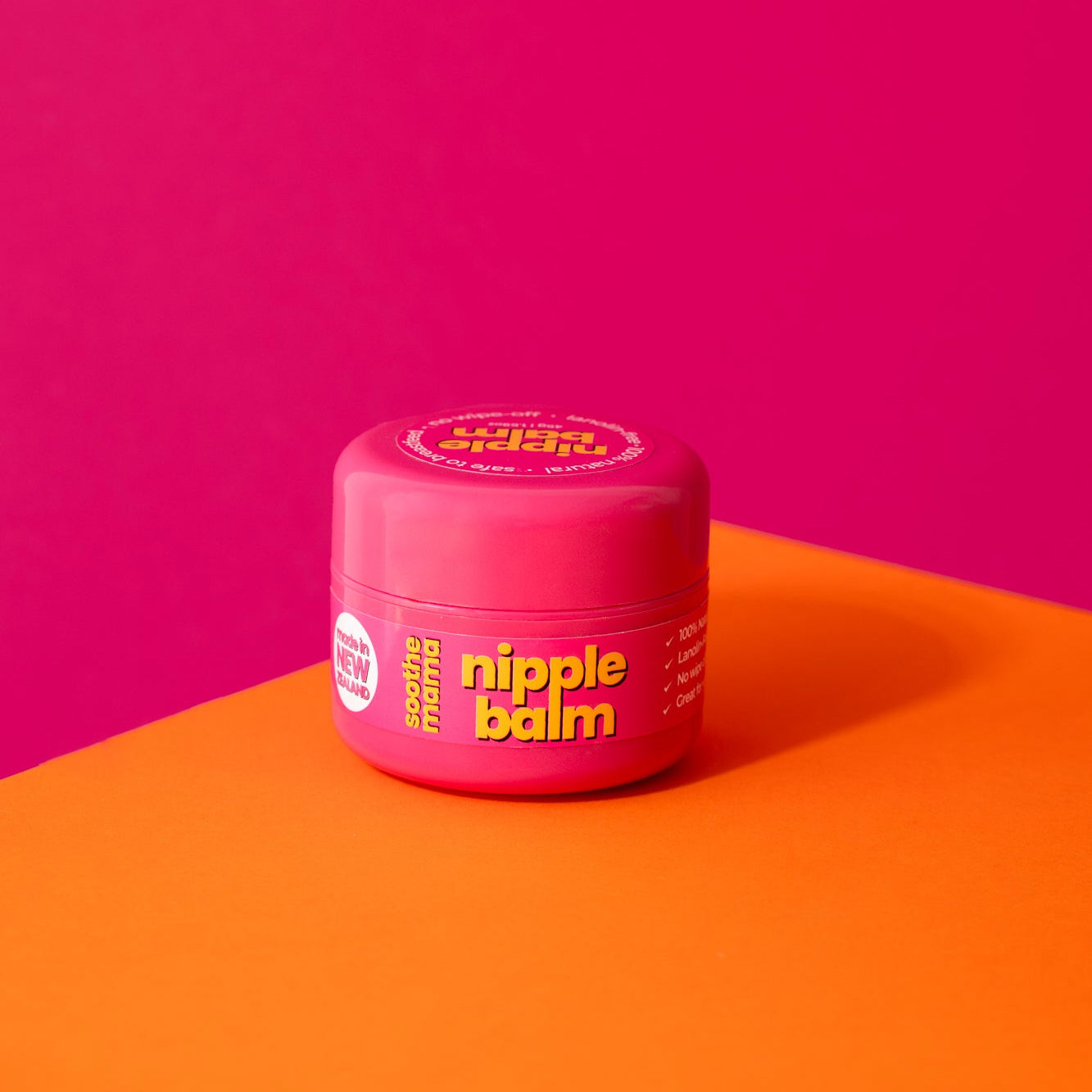 Pink jar of 'nipple balm' on a pink and orange background